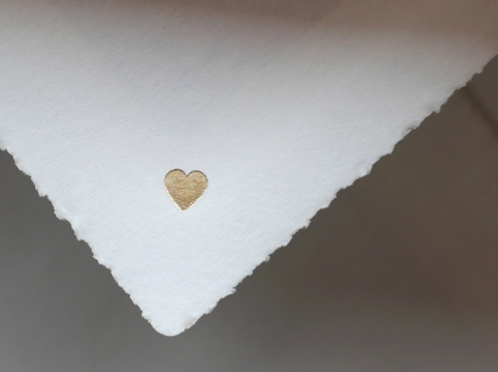 Diese exquisiten Einladungskarten auf cremeweißem Büttenpapier, veredelt mit mattgoldener Herzprägung, werden von einem blau gefütterten Umschlag ergänzt.