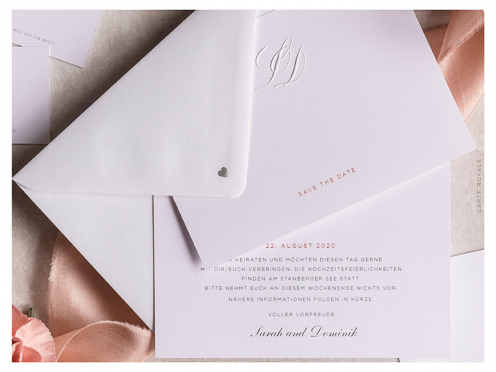 Mit persönlichem Monogramm geprägte Save-the-Dates, gedruckt auf weißem GMUND Papier. Ein silbernes Herz schmückt die Rückseite des Briefumschlags.