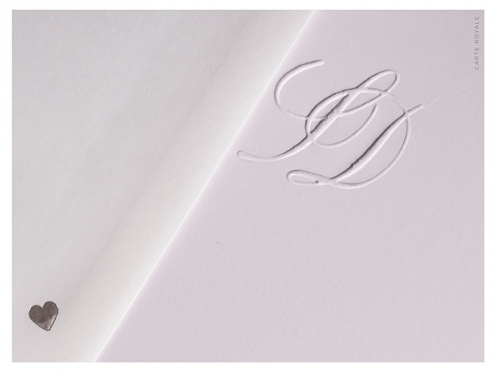 Mit persönlichem Monogramm geprägte Save-the-Dates, gedruckt auf weißem GMUND Papier. Ein silbernes Herz schmückt die Rückseite des Briefumschlags.