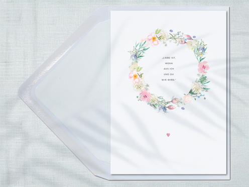 Für Hochzeiten in zarten Tönen: Ein pastellfarbener Blütenkranz und ein pink-pastell geprägtes Herz auf edlem Papier setzen stilvolle Akzente – ein haptisches und visuelles Erlebnis.
