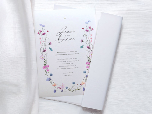 Die Hochzeitseinladung vereint zarte pastellige Blumenranken, minimalistische Typografie und ein silbernes Herz als handgeprägtes Detail – elegant, romantisch und zeitlos.