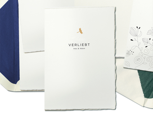 Moderne Hochzeitseinladung mit geradliniger Sans-Serif-Schrift und goldgeprägten Libelle, die als Symbol für Liebe und Veränderung steht.