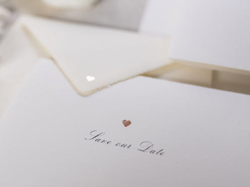 Auf Büttenpapier gedruckte Save-the-Date Karte zur Hochzeit mit rosé goldener Prägung.