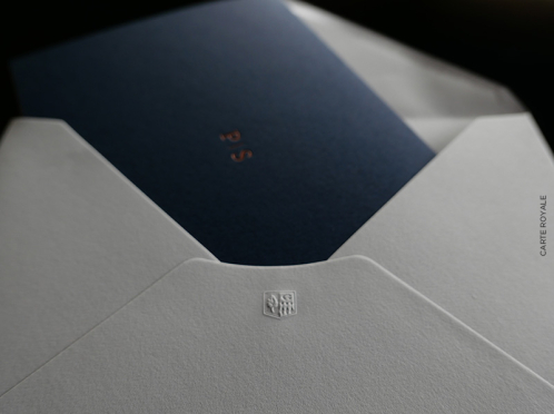 Royale Einladung, gedruckt und in Kupfer geprägt auf Gmund-Papier, umhüllt von einer royalblauen Klappkarte und verpackt in einem edlen Cotton-Briefumschlag.