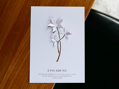 Stilvolle Hochzeitseinladung mit ausgestanztem Blumenmotiv – weiß auf weiß, mit feiner Typografie für zeitlose Eleganz.