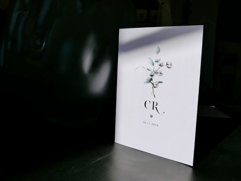 Hochwertige Hochzeitsfotografie einer Hochzeitseinladung mit Initialen, geprägtem Herz in Silber und Eucalyptus Aquarell