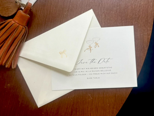 Moderne Save-the-Date Karten mit roségoldener Champagnerprägung und einer roségold geprägten Schleife auf der Umschlagspitze – stilvoll gestaltet und von Hand im Atelier Carte Royale veredelt.