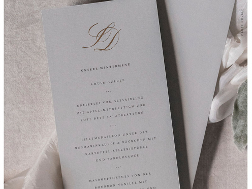 Die elegante Hochzeitsmenükarte besticht mit goldgeprägten Initialen, gedruckt auf edlem grauen GMUND-Papier. Diese Kombination aus kühler Eleganz und warmem Gold verleiht Ihrer Hochzeit eine zeitlose Note.