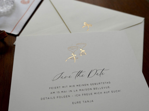 Moderne Save-the-Date Karten mit roségoldener Champagnerprägung und einer roségold geprägten Schleife auf der Umschlagspitze – stilvoll gestaltet und von Hand im Atelier Carte Royale veredelt.