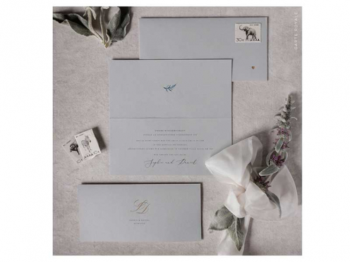 Erleben Sie elegante Einladungen zur Hochzeit mit Ihrem individuellen Monogramm in Goldprägung auf edlem grauem Papier. Der Briefumschlag, verziert mit einem goldenen Herz, ergänzt den exklusiven Look perfekt.