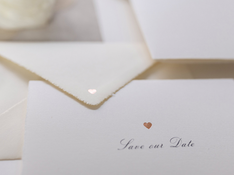 Auf Büttenpapier gedruckte Save-the-Date Karte zur Hochzeit mit rosé goldener Prägung.