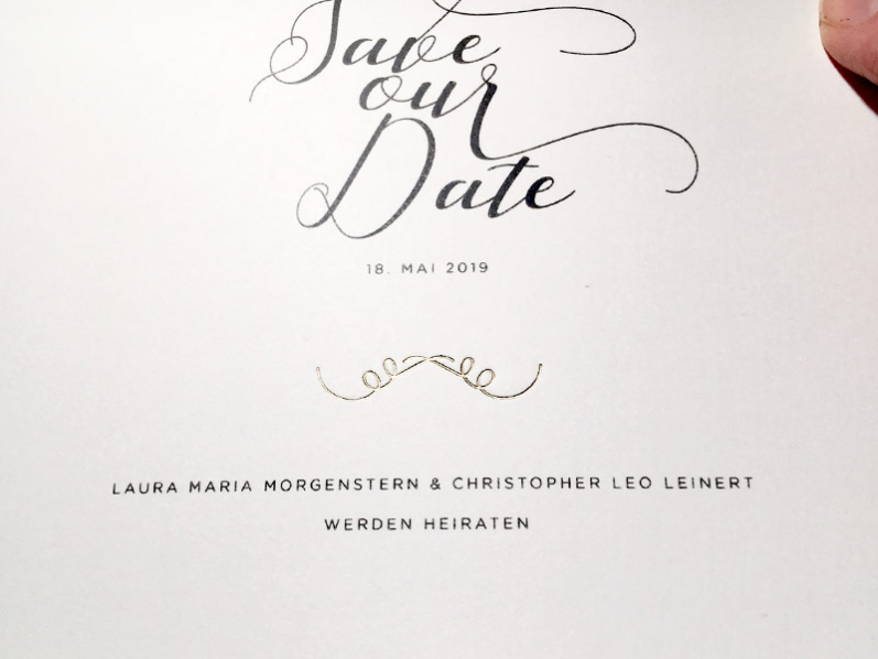 Kalligrafie Save-the-Date Karten gedruckt auf quadratischem Büttenpapier mit gold geprägtem Ornament.